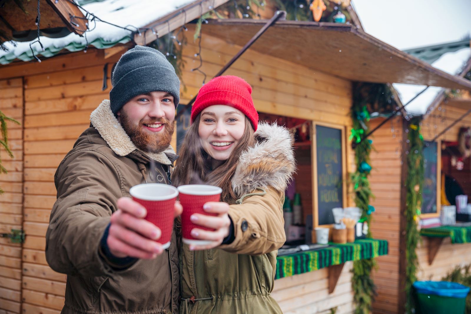 Happy couple offering hot drinks to you on christmas market